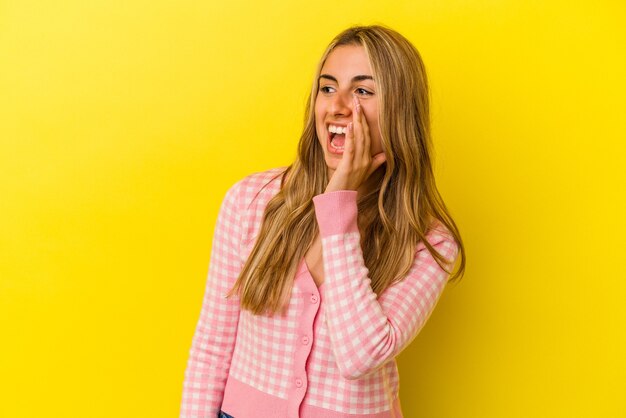 Joven mujer caucásica rubia aislada en la pared amarilla gritando emocionado al frente