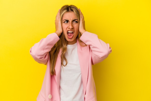 Joven mujer caucásica rubia aislada en la pared amarilla que cubre los oídos con las manos tratando de no escuchar un sonido demasiado fuerte