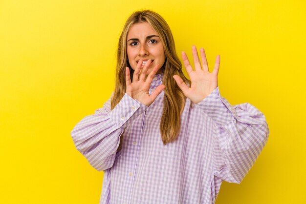 Joven mujer caucásica rubia aislada en la pared amarilla rechazando a alguien mostrando un gesto de disgusto