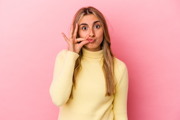 Joven mujer caucásica rubia aislada en la pared rosa con los dedos en los labios guardando un secreto