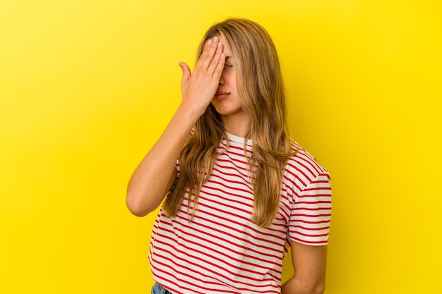 Joven mujer caucásica rubia aislada sobre fondo amarillo con dolor de cabeza, tocando la parte delantera de la cara.