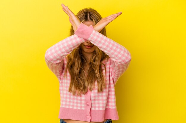 Joven mujer caucásica rubia aislada sobre fondo amarillo manteniendo dos brazos cruzados, concepto de negación.