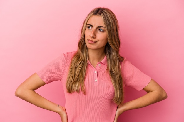 Joven mujer caucásica rubia aislada sobre fondo rosa confundida, se siente dudosa e insegura.