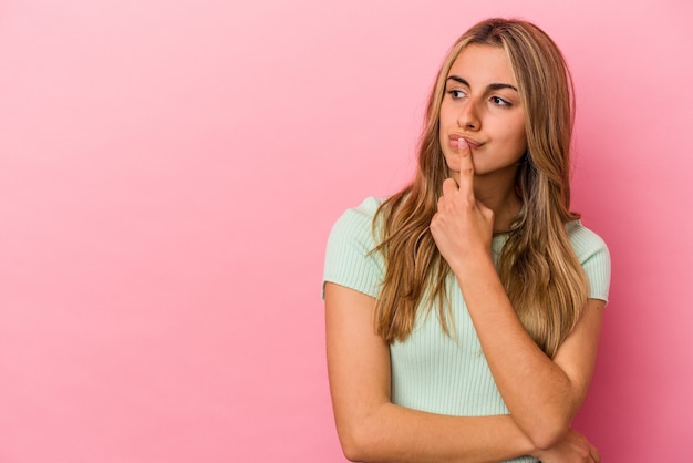 Joven mujer caucásica rubia aislada sobre fondo rosa mirando hacia los lados con expresión dudosa y escéptica.