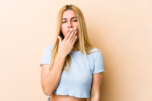 Joven mujer caucásica rubia bostezando mostrando un gesto cansado cubriendo la boca con la mano.