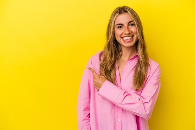 Joven mujer caucásica rubia sonriendo y apuntando a un lado, mostrando algo en el espacio en blanco.