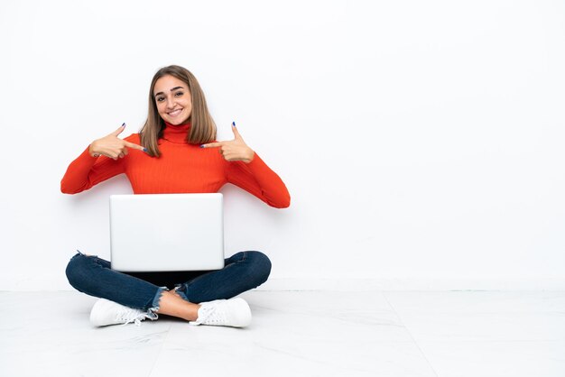 Joven mujer caucásica sentada en el suelo con una computadora portátil orgullosa y satisfecha de sí misma