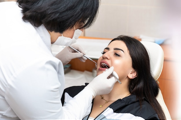 Joven mujer caucásica sentado en el sillón dental en el centro médico mientras médico profesional arregla sus dientes