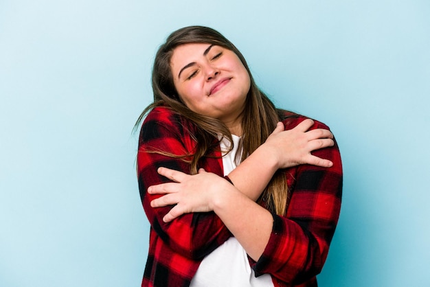 Foto joven mujer caucásica con sobrepeso aislada de fondo azul abraza sonriendo despreocupada y feliz