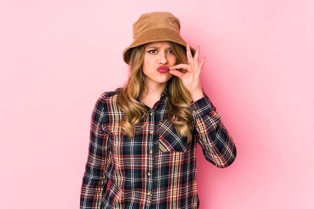 Joven mujer caucásica con sombrero aislado con los dedos en los labios guardando un secreto.