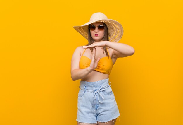 Joven mujer caucásica con un sombrero de paja, look de verano mostrando un gesto de tiempo de espera.