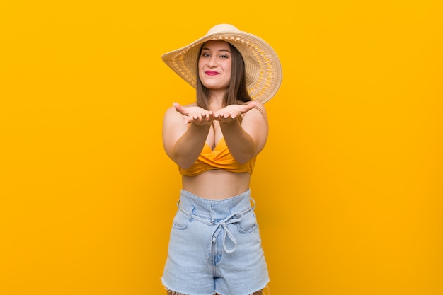 Joven mujer caucásica con un sombrero de paja, look de verano sosteniendo algo con palmeras