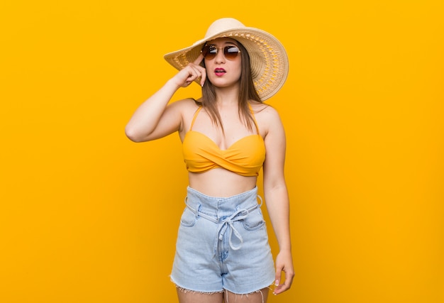 Joven mujer caucásica con un sombrero de paja, mirada de verano mostrando un gesto de decepción con el dedo índice.