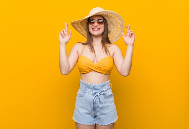 Foto joven mujer caucásica con un sombrero de paja, verano mira cruzar los dedos para tener suerte