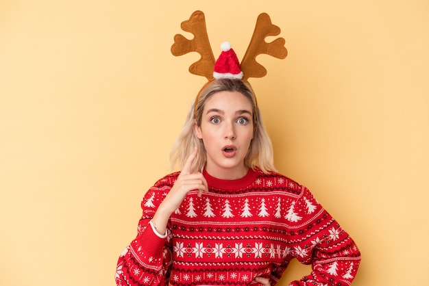 Joven mujer caucásica con un sombrero de reno de Navidad aislado sobre fondo amarillo con una idea, concepto de inspiración.