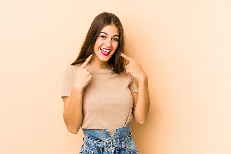 Foto joven mujer caucásica sonríe, señalando la boca con el dedo.
