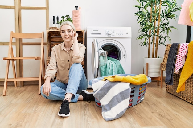 Joven mujer caucásica sonriendo confiada haciendo la ropa en la lavandería