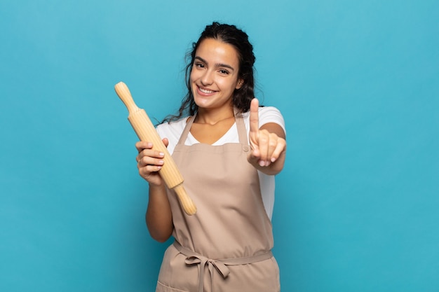 Joven mujer caucásica sonriendo y mirando amistosamente, mostrando el número uno o primero con la mano hacia adelante, contando hacia atrás