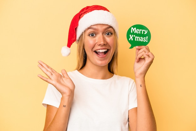 Joven mujer caucásica sosteniendo un apoyos de Navidad aislado sobre fondo amarillo