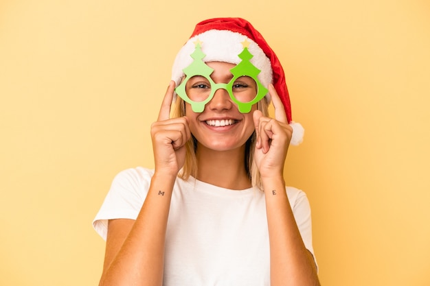 Joven mujer caucásica sosteniendo un apoyos de Navidad aislado sobre fondo amarillo