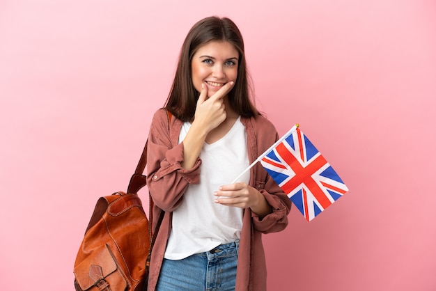 Joven mujer caucásica sosteniendo una bandera del Reino Unido aislada sobre fondo rosa feliz y sonriente