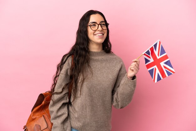 Joven mujer caucásica sosteniendo una bandera del Reino Unido aislada sobre fondo rosa pensando en una idea mientras mira hacia arriba