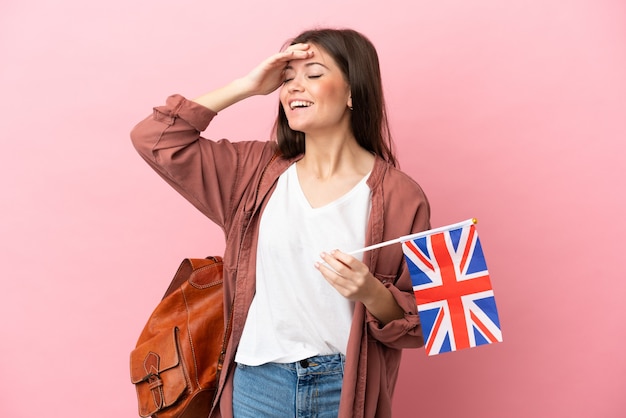 Joven mujer caucásica sosteniendo una bandera del Reino Unido aislada sobre fondo rosa sonriendo mucho