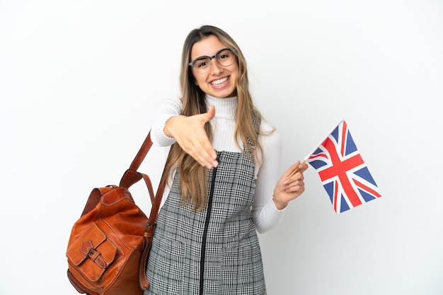 Joven mujer caucásica sosteniendo una bandera del Reino Unido aislado sobre fondo blanco un apretón de manos para cerrar un buen trato
