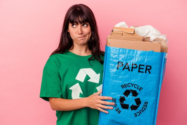 Joven mujer caucásica sosteniendo una bolsa de cartón reciclado aislada sobre fondo rosa confundida, se siente dudosa e insegura.