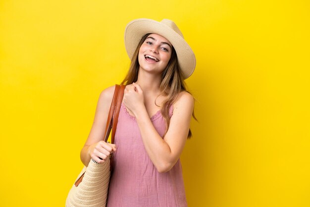 Joven mujer caucásica sosteniendo una bolsa de playa aislada de fondo amarillo celebrando una victoria