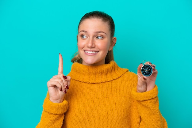 Joven mujer caucásica sosteniendo una brújula aislada de fondo azul con la intención de darse cuenta de la solución mientras levanta un dedo