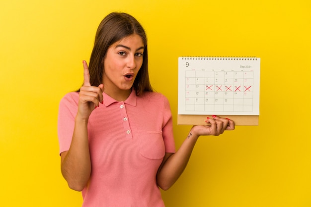 Joven mujer caucásica sosteniendo un calendario aislado sobre fondo amarillo con una idea, concepto de inspiración.