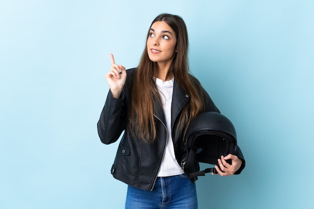 Joven mujer caucásica sosteniendo un casco de motocicleta aislado en azul apuntando hacia una gran idea