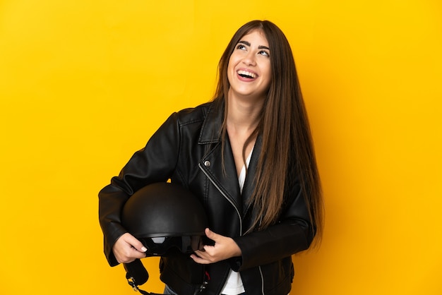 Joven mujer caucásica sosteniendo un casco de motocicleta aislado en la pared amarilla riendo