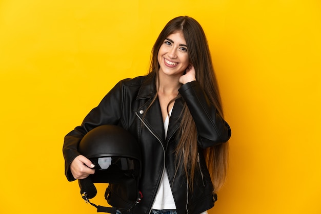 Joven mujer caucásica sosteniendo un casco de motocicleta aislado sobre fondo amarillo riendo