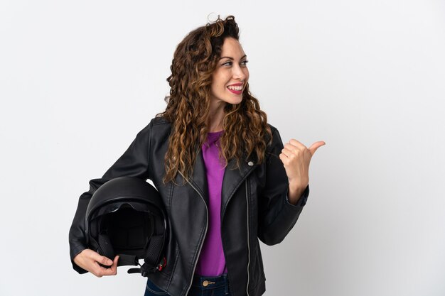 Joven mujer caucásica sosteniendo un casco de motocicleta apuntando hacia el lado para presentar un producto