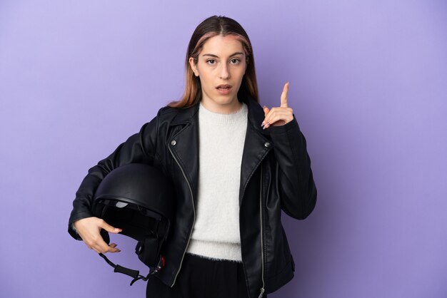 Joven mujer caucásica sosteniendo un casco de motocicleta en púrpura pensando en una idea apuntando con el dedo hacia arriba