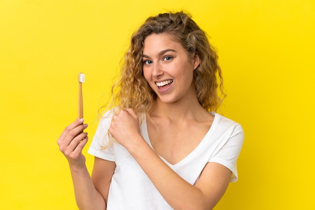 Joven mujer caucásica sosteniendo un cepillado de dientes aislado sobre fondo amarillo celebrando una victoria