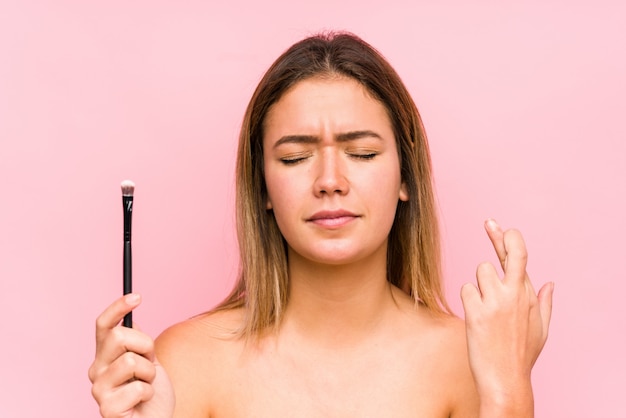 Joven mujer caucásica sosteniendo un cepillo de ojos cruzando los dedos