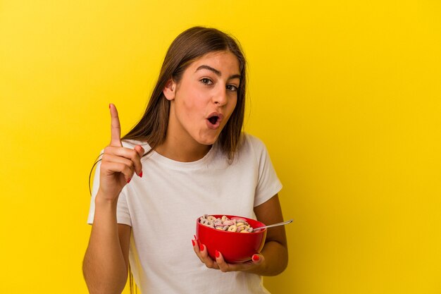 Joven mujer caucásica sosteniendo cereales aislado sobre fondo amarillo teniendo una idea, concepto de inspiración.