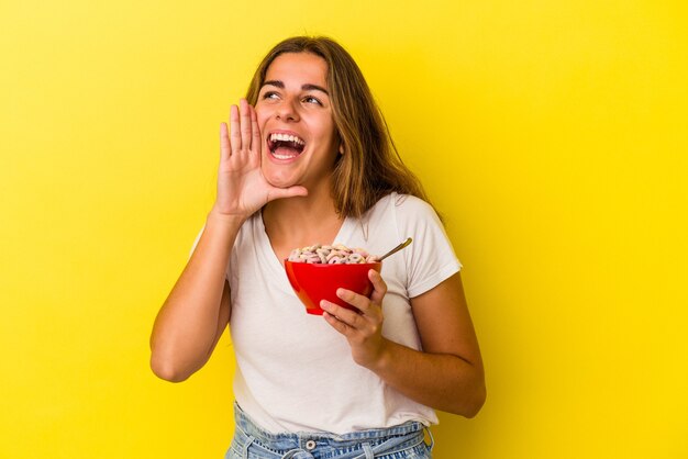 Foto joven mujer caucásica sosteniendo cereales aislados sobre fondo amarillo gritando y sosteniendo la palma cerca de la boca abierta.