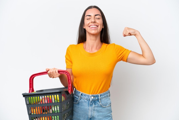 Foto joven mujer caucásica sosteniendo una cesta de la compra llena de comida aislada de fondo blanco haciendo un gesto fuerte