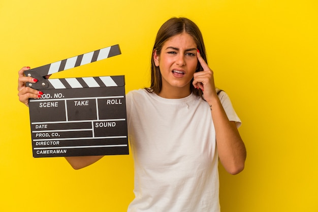 Joven mujer caucásica sosteniendo claqueta aislado sobre fondo blanco mostrando un gesto de decepción con el dedo índice.