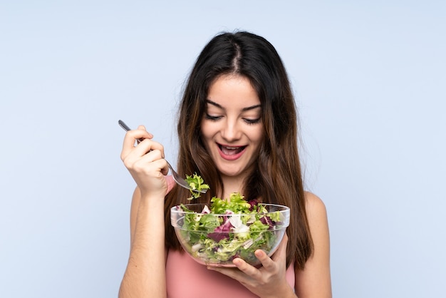 Joven mujer caucásica sosteniendo una ensalada aislada en azul