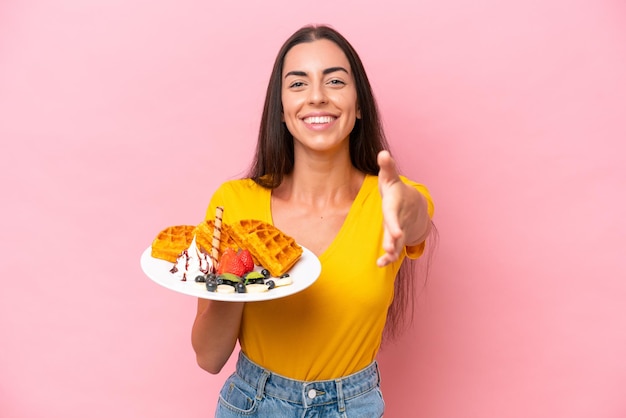 Foto joven mujer caucásica sosteniendo gofres aislados en un fondo rosado dándose la mano para cerrar un buen trato