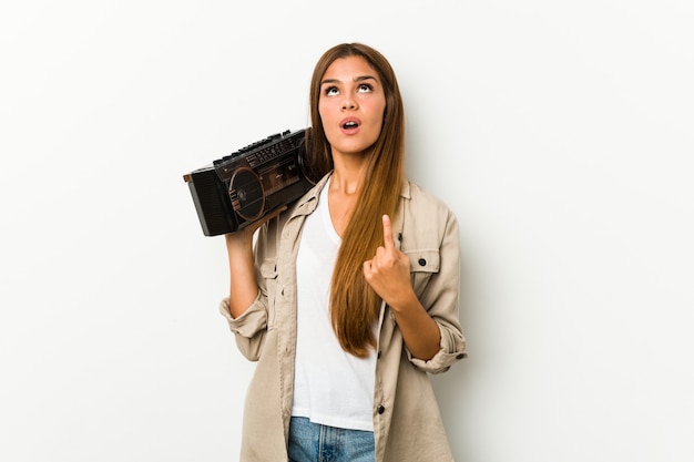 Joven mujer caucásica sosteniendo un guetto blaster apuntando hacia arriba con la boca abierta.