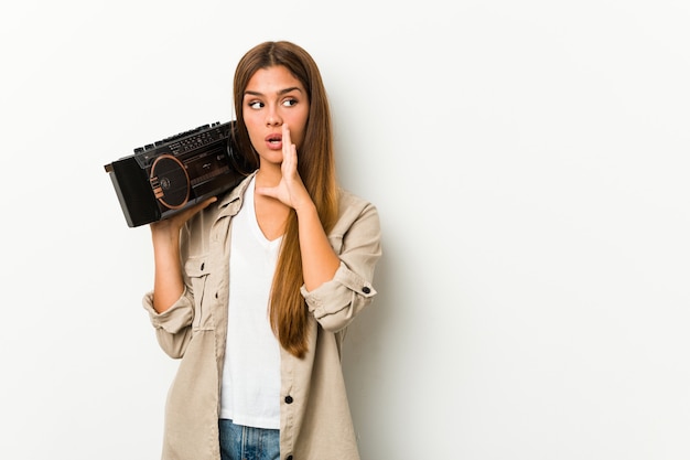 Joven mujer caucásica sosteniendo un guetto blaster está diciendo una noticia secreta de frenado en caliente y mirando a un lado