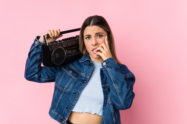 Joven mujer caucásica sosteniendo un guetto blaster morderse las uñas, nervioso y muy ansioso.