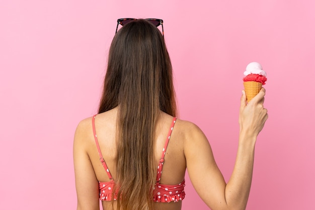 Joven mujer caucásica sosteniendo un helado aislado sobre fondo rosa en posición trasera