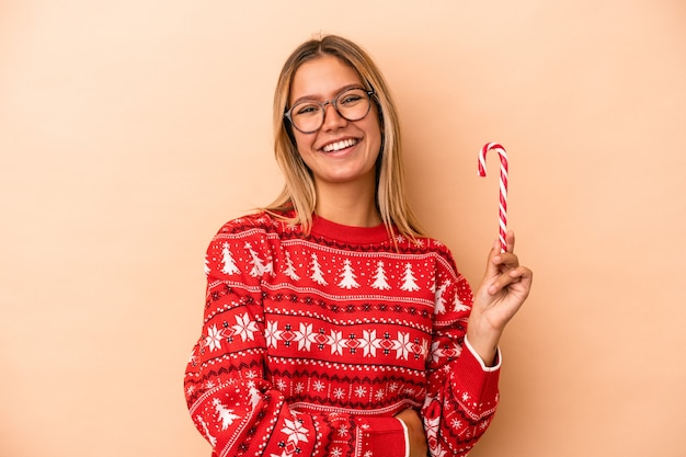 Joven mujer caucásica sosteniendo un palo de Navidad aislado sobre fondo beige riendo y divirtiéndose.